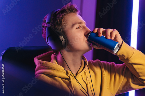 Young professional cybersport gamer playing online video game late at night, drinking caffeine energy drink to wake up and concentrate, focus on multiplay tournament. Games addiction concept photo