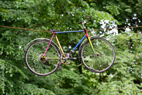 A colorful bicycle hung on wires among the trees in the park.