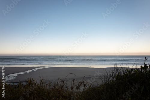 Beautiful shot of forest trees in Heaphy Beach, New Zealand with mountains and sunset sky on horizon photo