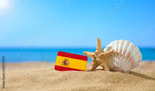 Tropical beach with seashells and Spain flag. The concept of a paradise vacation on the beaches of Spain.