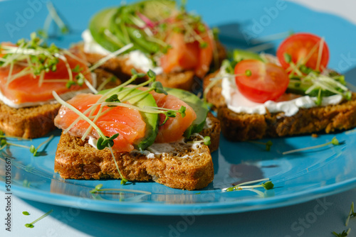closeup toast with salmon, micro greens, open sandwich with fish, healthy snack on blue plate