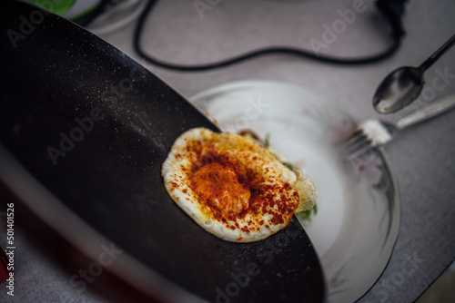 Closeup shot of a transfering fried eggs with paprika from the pan to a plate photo
