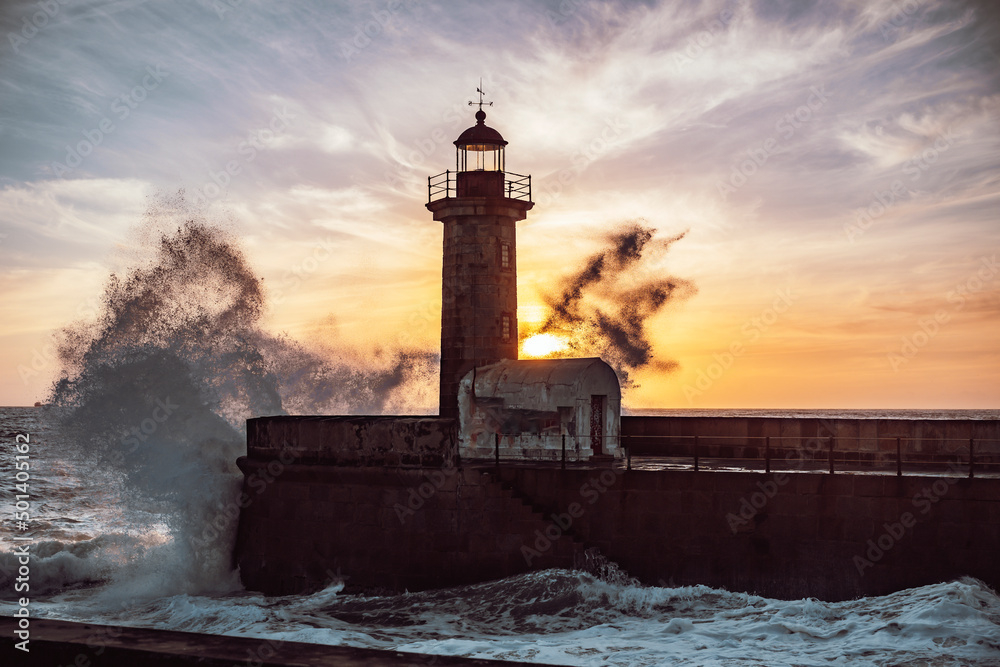 Waves of the sea breaking over the Porto lighthouse with the sunset in the background