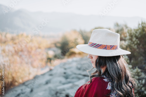 Traditional latin american woman wearing a red poncho and a hat seen from behind, in a natural space. Womens empowerment