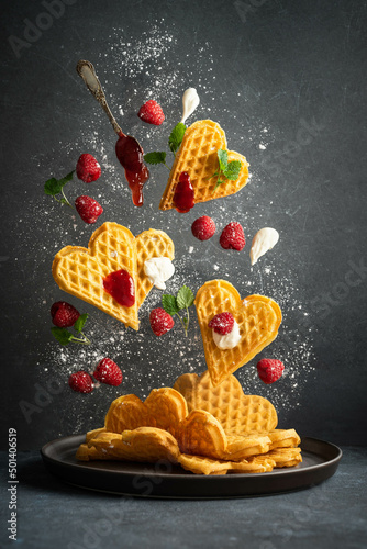 Creative photo of norwegian heart shaped waffles with raspberries and cream. Flying waffles. Levitation