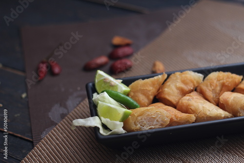 Fried spring rolls in a black plate served with tamarind sauce on a black wooden table