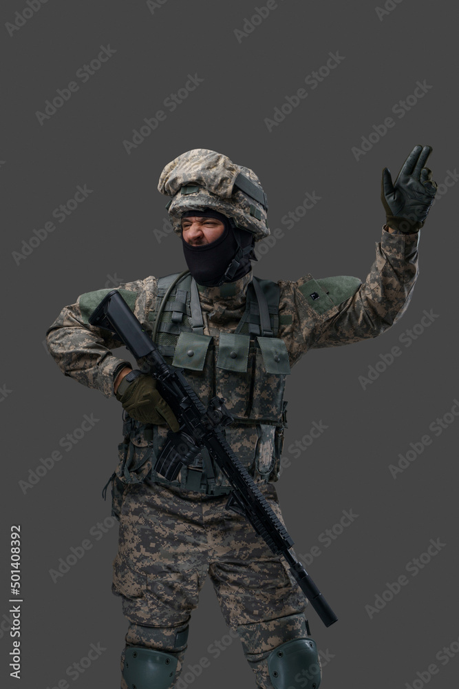 Proud serviceman dressed in camouflage clothes with rifle gesturing against grey background. Proud serviceman dressed in camouflage clothes with rifle gesturing against grey background.