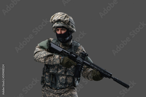 Fototapet Shot of handsome soldier dressed in modern military uniform holding rifle against grey background