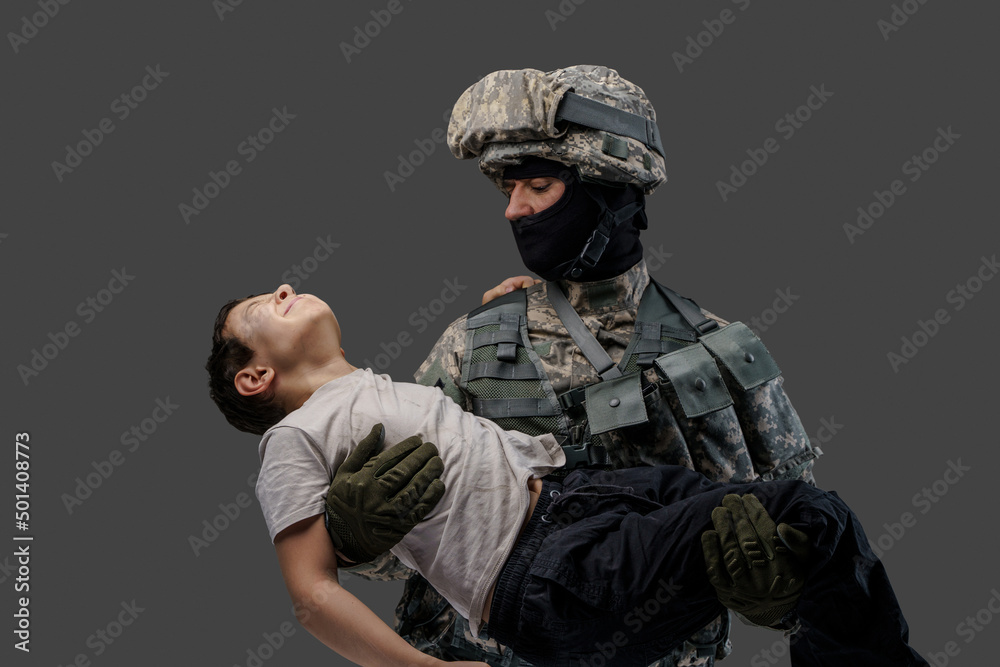Fototapeta premium Shot of professional army man saving wounded little boy against grey background.