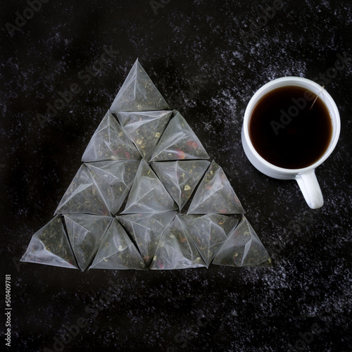 Pyramid tea bags with green flavored tea with fruit and a white mug on the dark textured surface of the kitchen table. Pyramid shape