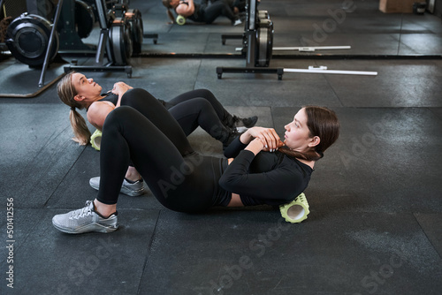 Midget woman and her trainer sitting at the floor and pump the press at the gym