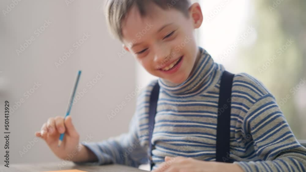 Smiling excited autistic child drawing as woman pointing talking. Portrait of happy confident Caucasian boy with mental illness studying at home with mother. Autism and family concept Smiling excited autistic child drawing as woman pointing talking. Portrait of happy confident Caucasian boy with mental illness studying at home with mother. Autism and family concept