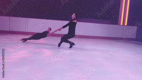 Pair of figure skaters rotate, go into death spiral,female partner hovers in air parallel to ice, man holds her hands.Figure skating element, dance support,slow motion,camera swings diagonally around. photo