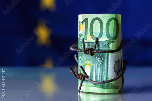 European Union currency wrapped in barbed wire against flag of EU as symbol of Economic warfare, sanctions and embargo busting. Selective focus on barbed wire. Copy space. photo