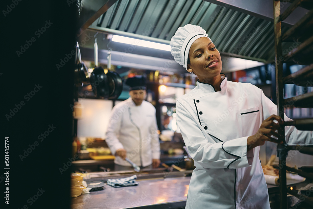 Happy black woman working as professional cook in restaurant.
