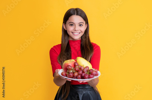 positive girl hold fresh fruit plate on yellow background. selective focus