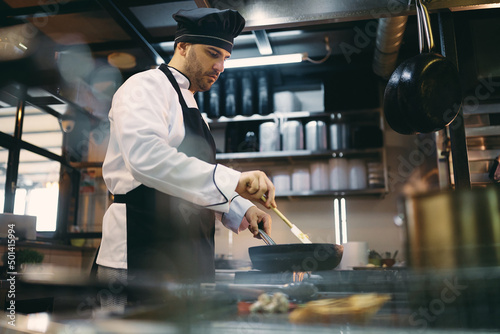 Professional cook prepares meal while working in the kitchen at restaurant.