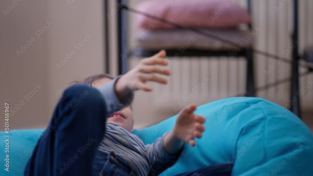 Portrait of autistic cheerful boy playing with teddy bear laughing lying on bag chair at home. Happy excited Caucasian child with mental disorder having fun enjoying leisure indoors Portrait of autistic cheerful boy playing with teddy bear laughing lying on bag chair at home. Happy excited Caucasian child with mental disorder having fun enjoying leisure indoors