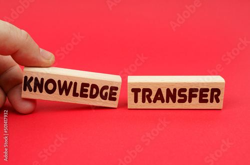 On a red background, wooden blocks, one of them in hand. The blocks are written - KNOWLEDGE TRANSFER