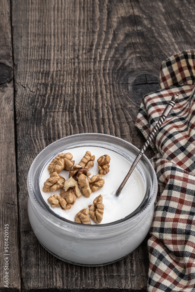Fresh natural homemade organic yogurt with walnuts in a glass jar on wooden table Fresh natural homemade organic yogurt with walnuts in a glass jar on wooden table