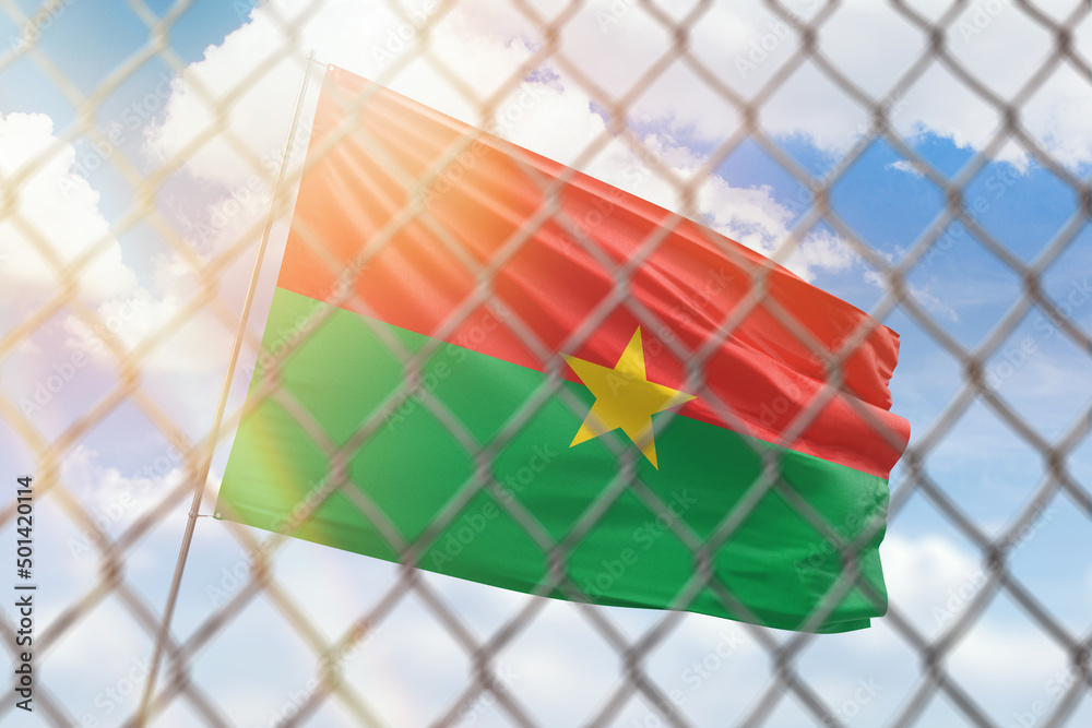 A steel mesh against the background of a blue sky and a flagpole with the flag of burkina faso