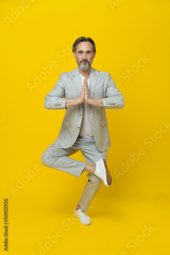 Balancing zen middle aged business man with hands put together looking at camera isolated on yellow background. Handsome mature businessman in white suit. Business concept. Copy space.