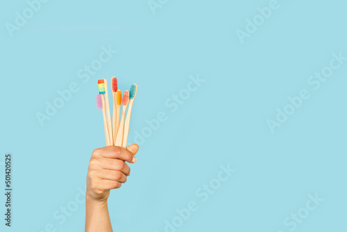 Mano de mujer sosteniendo un  conjunto de cepillos de dientes de bambú sobre un fondo celeste liso y aislado. Vista de frente y de cerca. Copy space. Concepto: salud photo