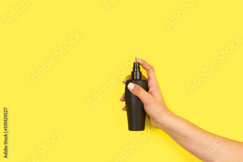 Mano de mujer sosteniendo un bote de spray negro sobre un fondo amarillo liso y aislado. Vista de frente y de cerca. Copy space photo