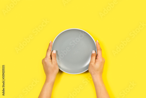 Canvastavla Manos de mujer sosteniendo un plato gris sobre un fondo brillante amarillo liso y aislado