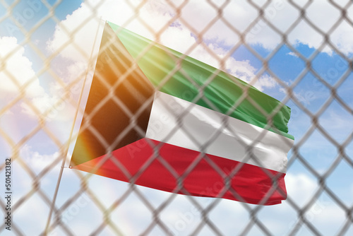 A steel mesh against the background of a blue sky and a flagpole with the flag of kuwait