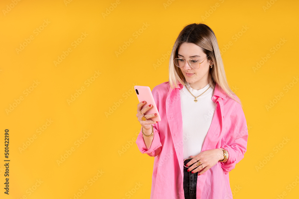 Young woman standing using her cell phone on yellow background Young woman standing using her cell phone on yellow background