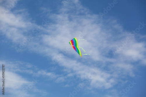 Blue sky with clouds. Summer day. Colorful rainbow kite hovers in the air high in the sky