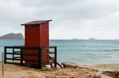 quiet, peaceful and calm scene. has a Red lifeguard beach shack. is a cloudy day in IBIZA. there is no one on the photography © GonzaloVega