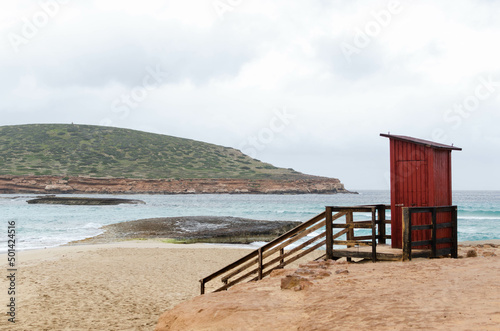 quiet, peaceful and calm scene. has a Red lifeguard beach shack on the right. is a cloudy day in IBIZA. there is no one on the beach © GonzaloVega