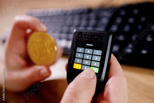 Close up womans hand holding bitcoin and cryptocurrencey hardware cold wallet on keybord background. Secure cryptocurrency storage photo