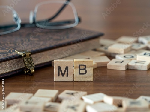 the acronym mb for management board word or concept represented by wooden letter tiles on a wooden table with glasses and a book photo