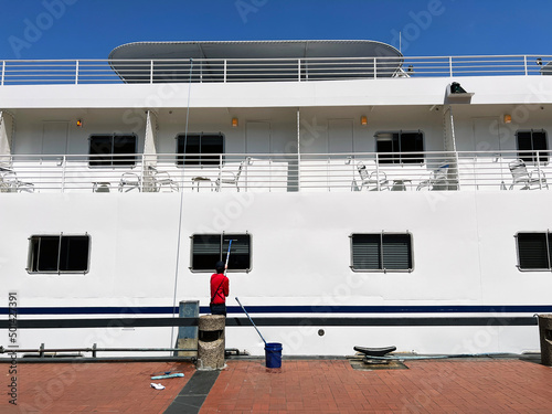 A lone maintenance worker paints the side of a cruise ship while docked in port.