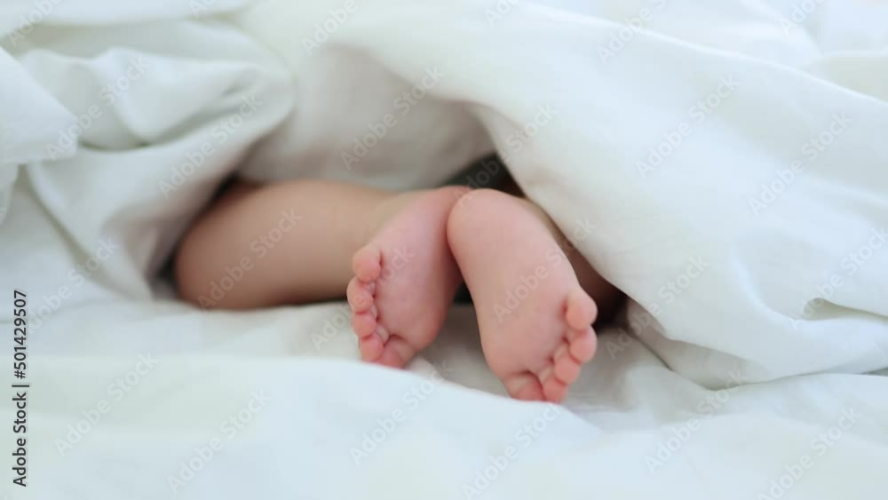 close-up bare feet and toes of infant baby legs in white sheet. newborn tiny fingers feet moving. caucasian little baby foot macro view. barefoot child legs close-up bare feet and toes of infant baby legs in white sheet. newborn tiny fingers feet moving. caucasian little baby foot macro view. barefoot child legs