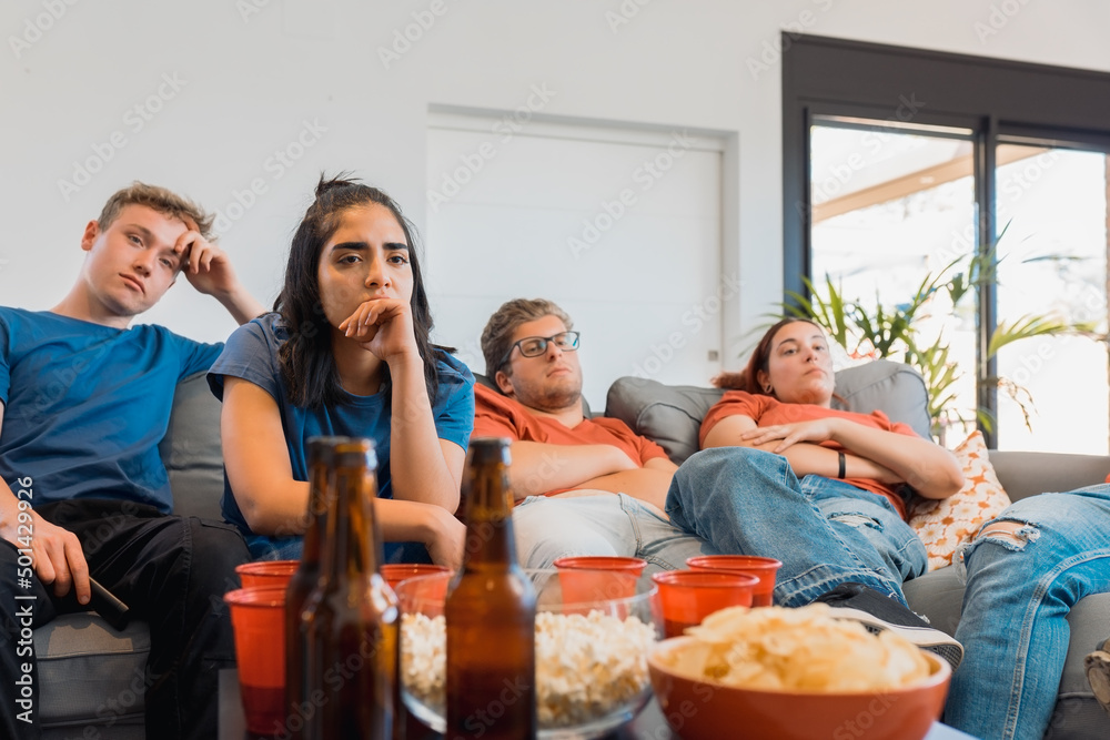 sad friends watching TV because their football team lost the game. upset young people at a house party. sad friends watching TV because their football team lost the game. upset young people at a house party.