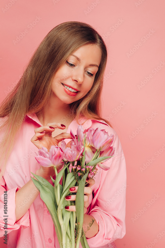 A sweet charming woman with flowers in a pink dress on a pink background smiles, happiness and luck