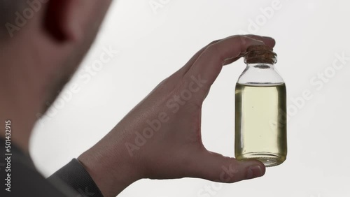 A man holds a small glass jar in his hand. There is a yellow liquid in the vessel. 
 photo