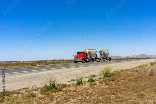 Photography Red semi-truck pulling a double dry bulk trailer on a rural highway in the Mojav