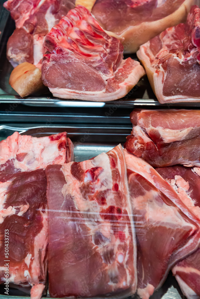 Variety of raw pork in display case of butcher market..