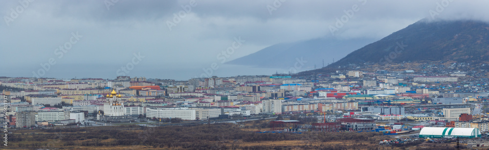 Panorama of the city of Magadan. Top view of the seaside town. Urban landscape with a cathedral, residential and administrative buildings. Cloudy rainy weather. Magadan region, Far East of Russia.