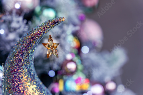 Crystal yellow star hanging on an iridescent mermaid glitter moon, pink green blue boker background, Christmas tree bauble photo