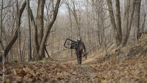 Gimbal following bowhunter in camouflage outfit walking in forest path during winter photo