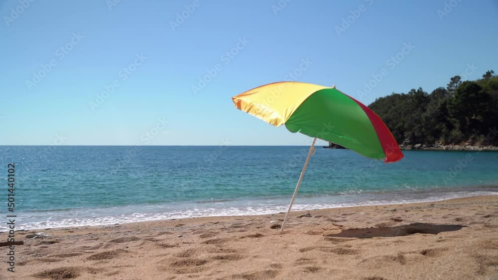 Beach with a bright colored sunshade against the backdrop of a bright blue sky and sea with waves. Tourist paradise Beach with a bright colored sunshade against the backdrop of a bright blue sky and sea with waves. Tourist paradise