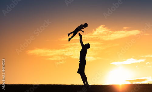  Happy parenting and raising children concept. Father holding up child to the sunset sky.