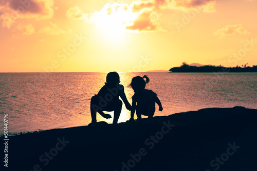 Silhouette of two children playing on the beach at sunset 