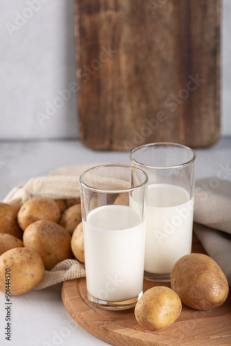 Vegan plant based milk in two transparent glasses. Alternative potato milk and potato tubers on gray table